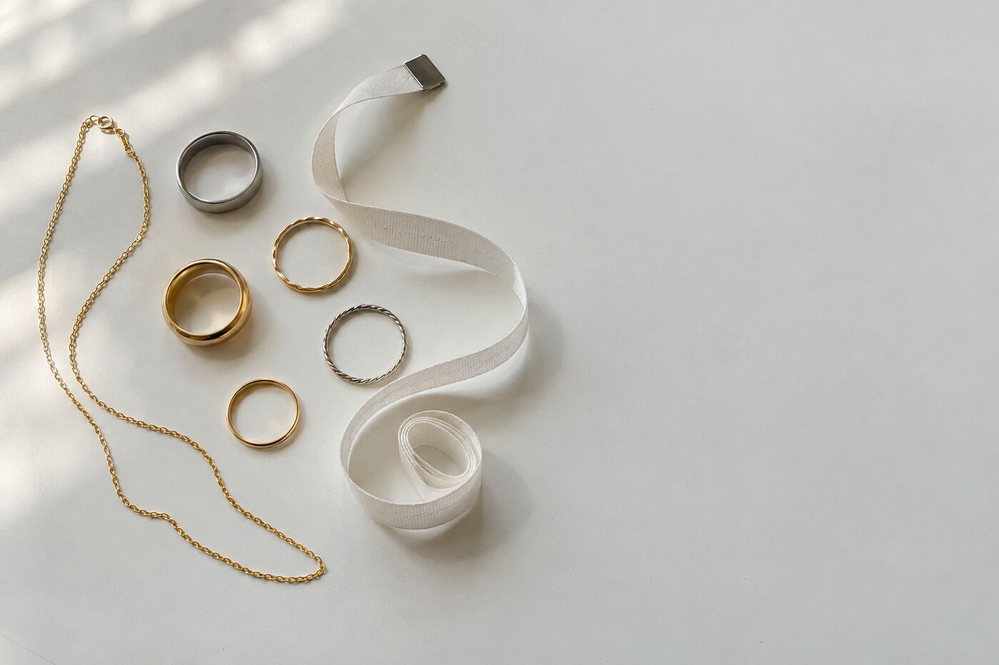 Losse ringen, een dunne gouden ketting en een papieren meetlint op een witte tafel