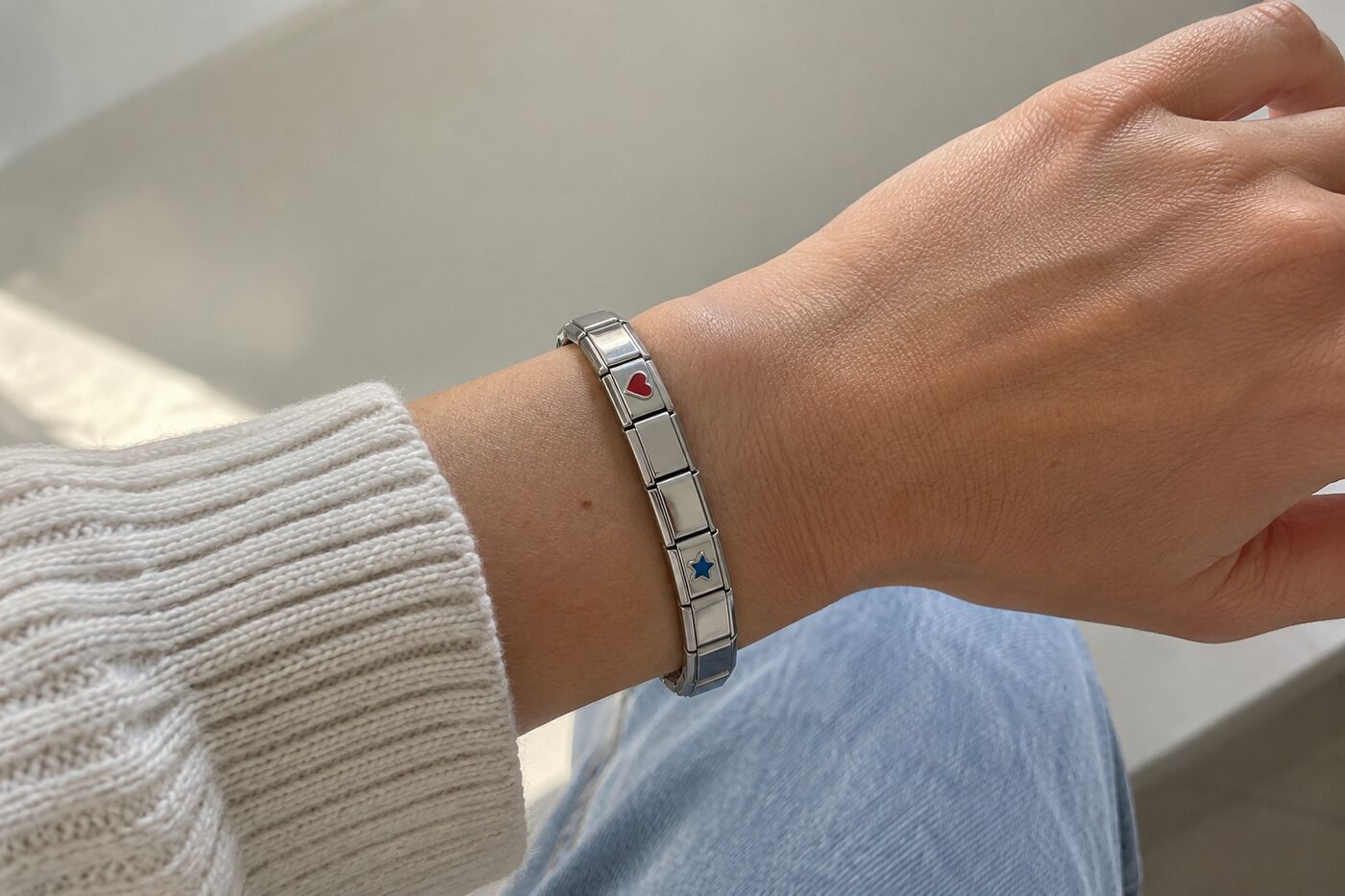 Pols met een Italian charm bracelet van platte stalen schakels, twee met een emaille hartje en sterretje