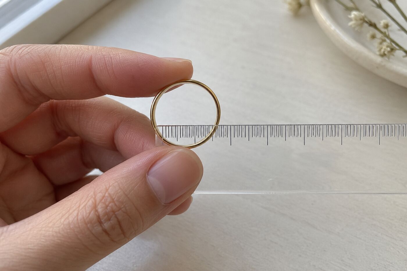 Hand houdt een dunne gouden ring tegen een doorzichtige liniaal om de binnendiameter af te lezen