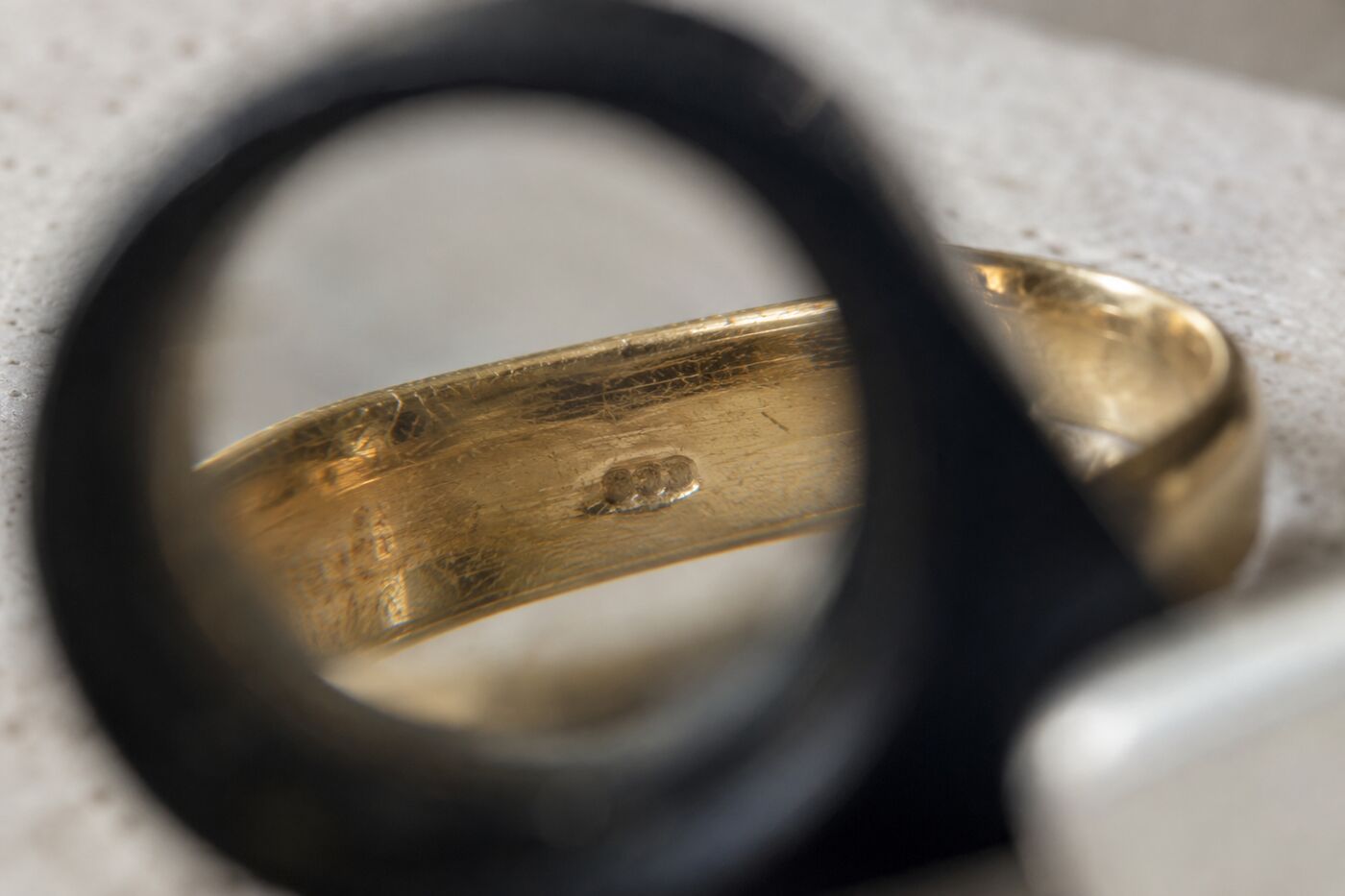 Binnenkant van een gouden ring onder een juweliersloep met een klein ingeslagen stempel