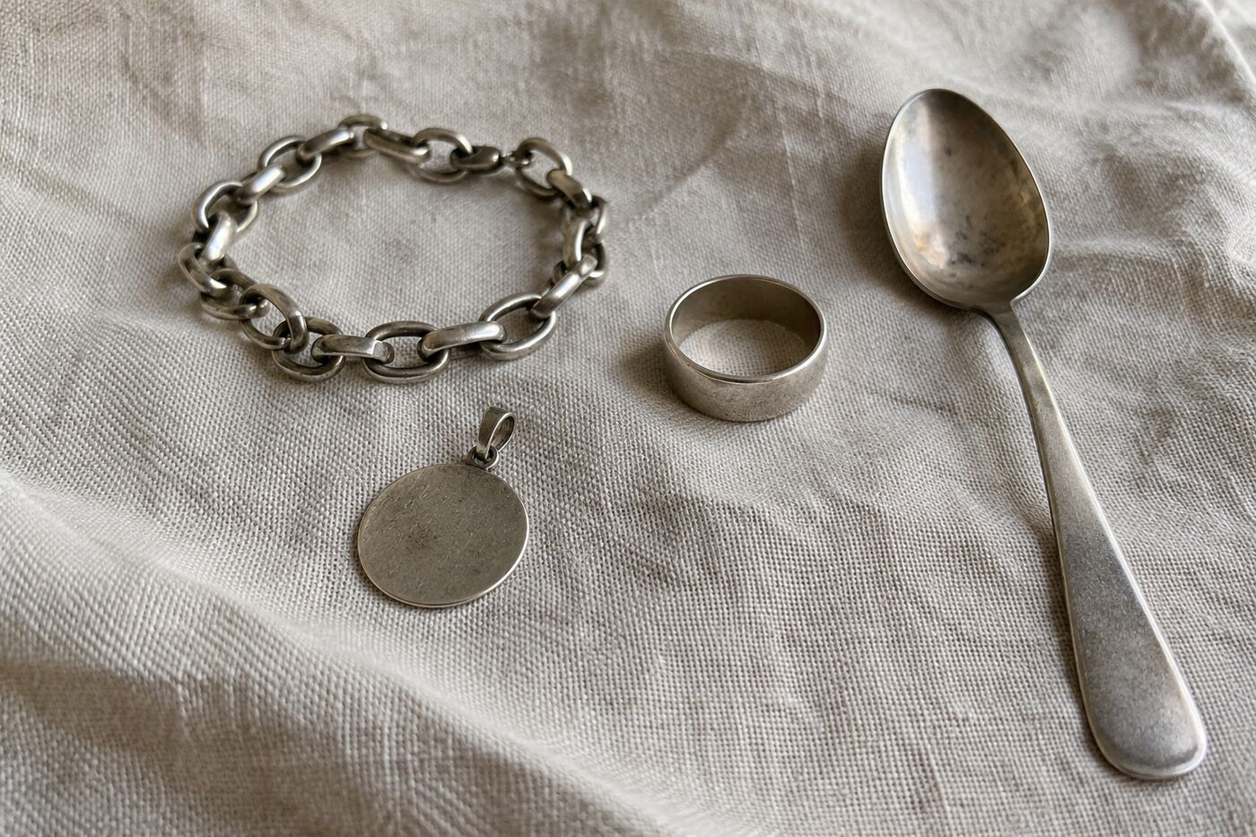 Zilveren schakelarmband, ring, hanger en een oud zilveren lepeltje op linnen